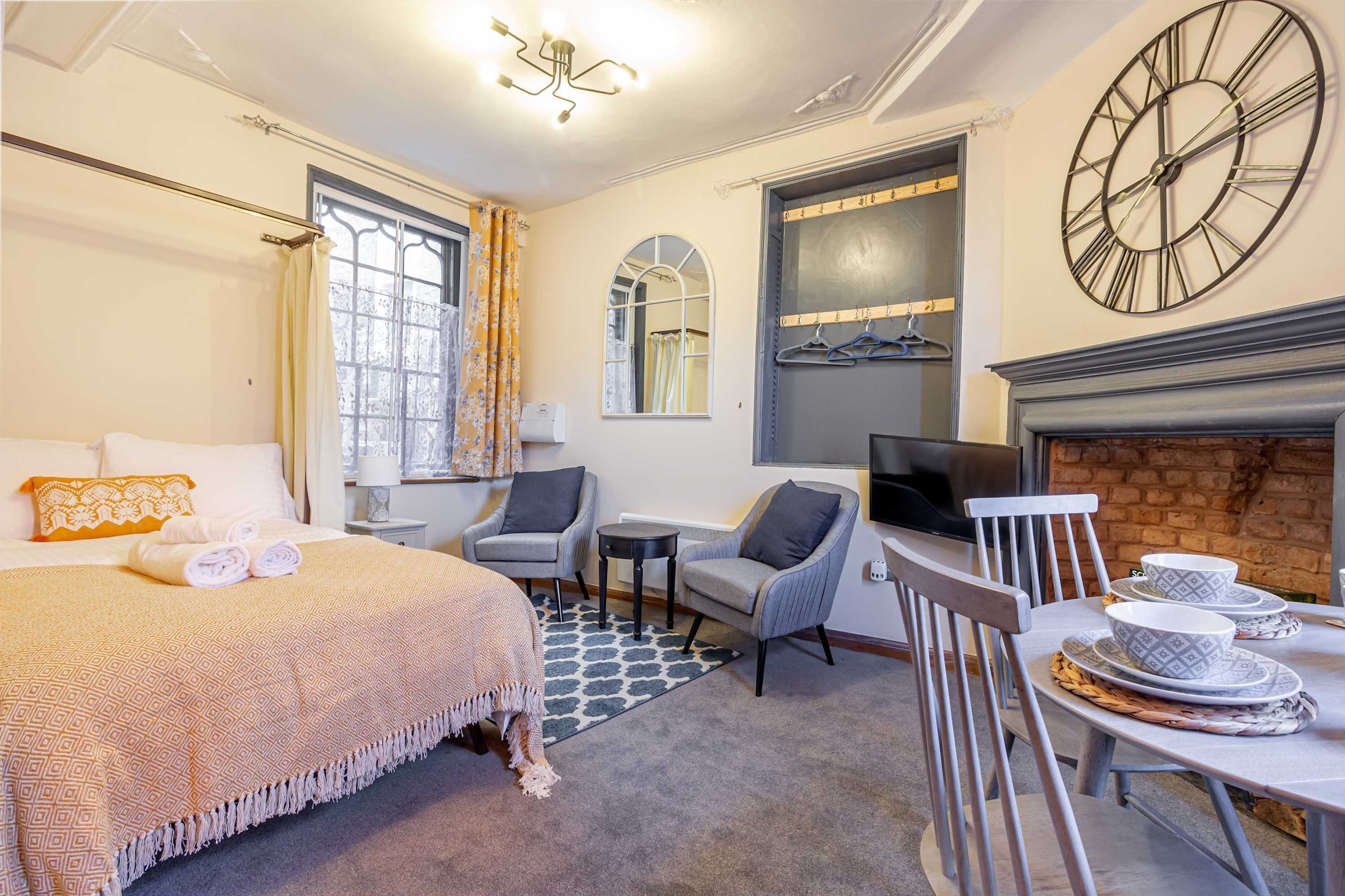 Une chambre d’hôtel comprenant un lit, deux fauteuils, une petite table, un téléviseur et une cheminée.