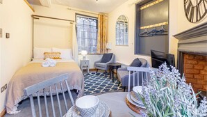Una camera d'albergo con un letto, un'area salotto con televisore, un camino e una finestra con tende.