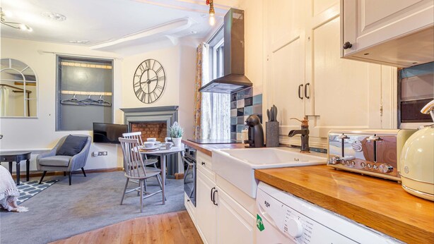 Una cucina moderna con mobili bianchi, forno a incasso, piano cottura e lavello. È presente un'area pranzo con tavolo e sedie, e un caminetto.