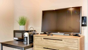 A modern room with a flat-screen TV, a coffee machine, a microwave, and a wooden cabinet.