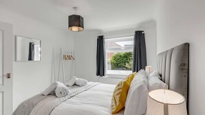 Une chambre d’hôtel avec un lit bien fait, une lampe de chevet, une fenêtre avec des rideaux et une vue sur la verdure.