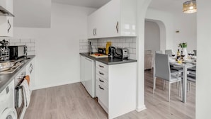 Une cuisine moderne avec des armoires blanches, un lave-vaisselle intégré et un coin repas avec une table dressée pour quatre personnes.