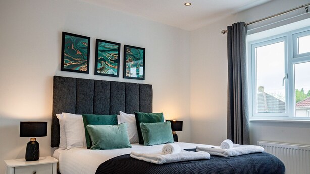 A neatly made bed with a dark headboard, green pillows, and a white blanket. There are two bedside tables with lamps, and a window with curtains. - Host Stay Carlisle Road House (Worcester)