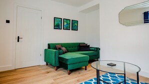 A room with a green sofa, a glass coffee table, and a blue patterned rug. There are three framed pictures on the wall and a mirror above the sofa. - Host Stay Carlisle Road House (Worcester)