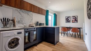 A modern kitchen with a built-in washer, oven, and dishwasher. There is a dining area with two chairs and a table. - Host Stay Carlisle Road House (Worcester)