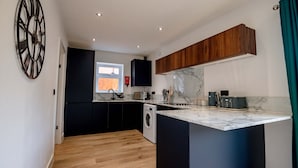 A modern kitchen with black cabinets, a marble countertop, and a washing machine. - Host Stay Carlisle Road House (Worcester)
