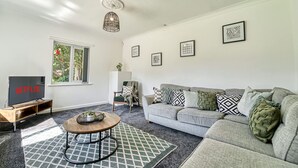 Ein Wohnzimmer mit grauem Sofa, einem Couchtisch, einem Fernseher und gerahmten Kunstwerken an der Wand.