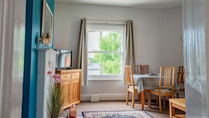 Ein Essbereich mit Tisch, Stühlen, einem Fenster mit Vorhängen, einem Schrank und einem Fernseher.