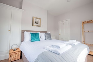 A neatly made bed with white linens and a striped blanket, a framed picture on the wall, and a wooden shelf unit to the right. - Host Stay Cannon Apartment (Worcester)