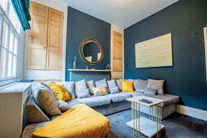 A modern living room with a grey sectional sofa, a yellow throw blanket, a small white coffee table, and a large mirror on the wall. - Host Stay Park Street Abode (Worcester)