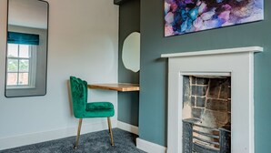 A room with a green velvet chair, a fireplace, a mirror, and a colorful abstract painting. - Host Stay Park Street Abode (Worcester)