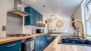 A modern kitchen with teal cabinets, a stainless steel range hood, a built-in oven, and a black sink. - Host Stay Park Street Abode (Worcester)