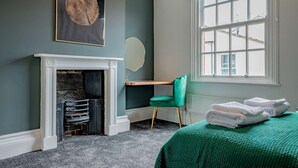 A room with a fireplace, a desk, a chair, a bed with a green bedspread, and a window with curtains. - Host Stay Park Street Abode (Worcester)