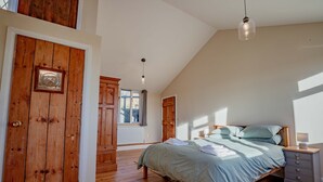 A bedroom with a wooden door, a bed with a green bedspread, a nightstand, and a hanging light fixture. - Host Stay Upperley Barn (Bromyard)