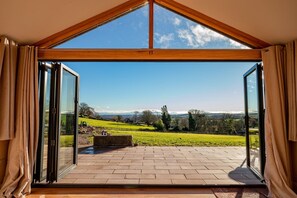 A room with a large glass door leading to a patio with a view of a green landscape and distant mountains. - Host Stay Upperley Barn (Bromyard)