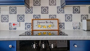 Uma cozinha com armários azuis, azulejos estampados e um quadro com a frase 'Squeeze the day'.