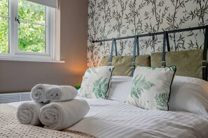 A neatly made bed with rolled towels, a window with a view of greenery, and a headboard with leaf-patterned pillows. - Host Stay Hales Orchard (Worcester)