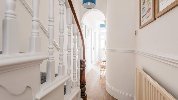 A staircase with white balusters and a wooden handrail, leading to a room with a radiator and a blue pendant light. - Host Stay The Haven at Church Road (Great Yarmouth)