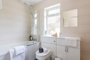 Une salle de bain moderne équipée d’une baignoire, de toilettes et d’une fenêtre laissant entrer la lumière naturelle.