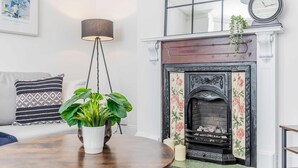A room with a fireplace, a clock, a framed artwork, a patterned pillow, and a potted plant. - Host Stay The Haven at Church Road (Great Yarmouth)