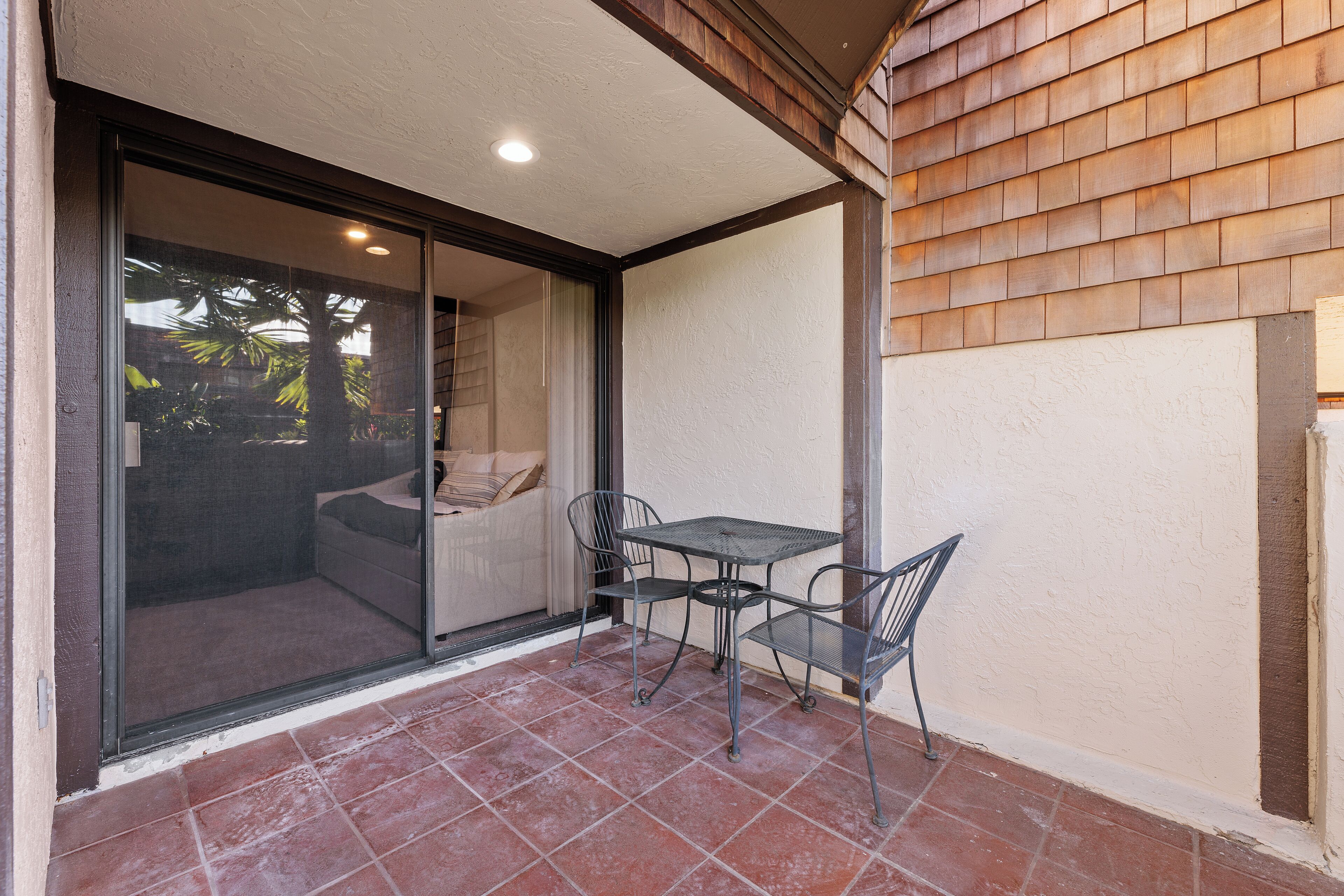 A patio with a table and chairs, a sliding glass door leading to a room, and a wooden shingled wall.