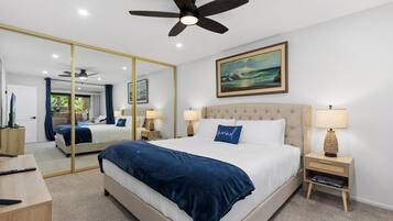 A hotel room with a large bed, a ceiling fan, a painting, a bedside table with a lamp, and a mirror.
