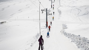 Une piste de ski avec des skieurs dévalant une pente douce, un télésiège en arrière-plan et un ciel dégagé.