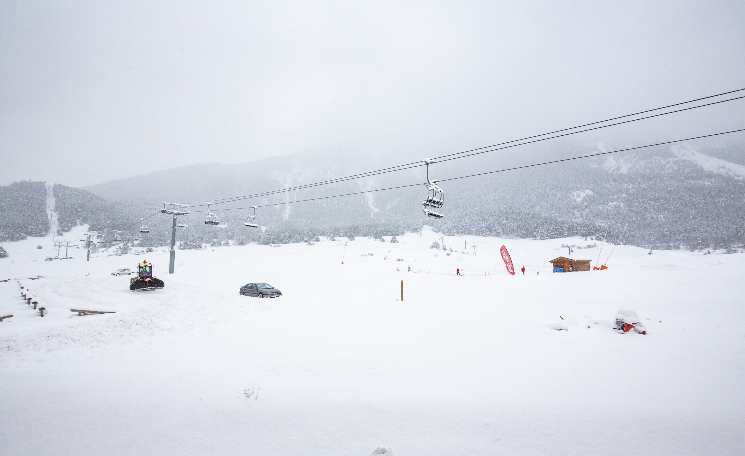 Pista de esquí nevada con telesilla, cabañas de madera y montañas al fondo.