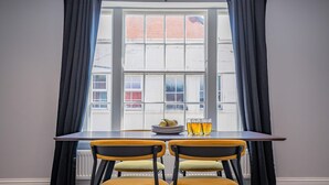 Ein Essbereich mit Tisch und Stühlen, einem Fenster mit Vorhängen und Blick auf Gebäude.