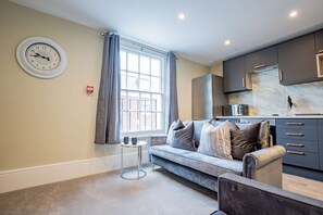 A modern living room with a sofa, a small side table, and a clock on the wall. - Host Stay Shaw Street Suite (Worcester)