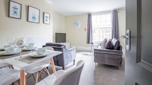 A modern living room with a dining area, grey sofas, a flat-screen TV, and a window with curtains. - Host Stay Shaw Street Suite (Worcester)