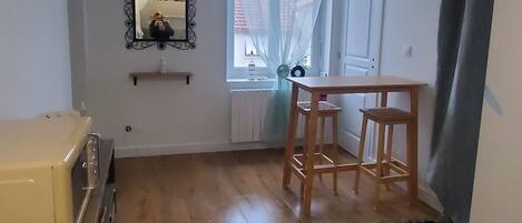 Ein Zimmer mit Holzboden, einem Esstisch mit Stühlen, einem Deckenventilator, einem Fenster mit Vorhängen und einem Heizkörper.