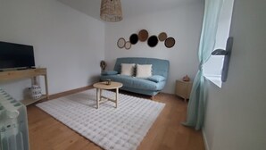 Un salon avec un canapé bleu, une petite table ronde, un tapis blanc et un téléviseur fixé au mur.