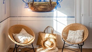 Une pièce comprenant deux fauteuils en osier, un pouf tressé et une fresque murale représentant des arbres et un paysage.