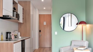 A modern kitchen with white cabinets, a built-in oven, and a coffee machine. There is a wooden door in the background and a round mirror on the wall. - w Radiant Loft w Balcony in Chapinero (Bogotá)