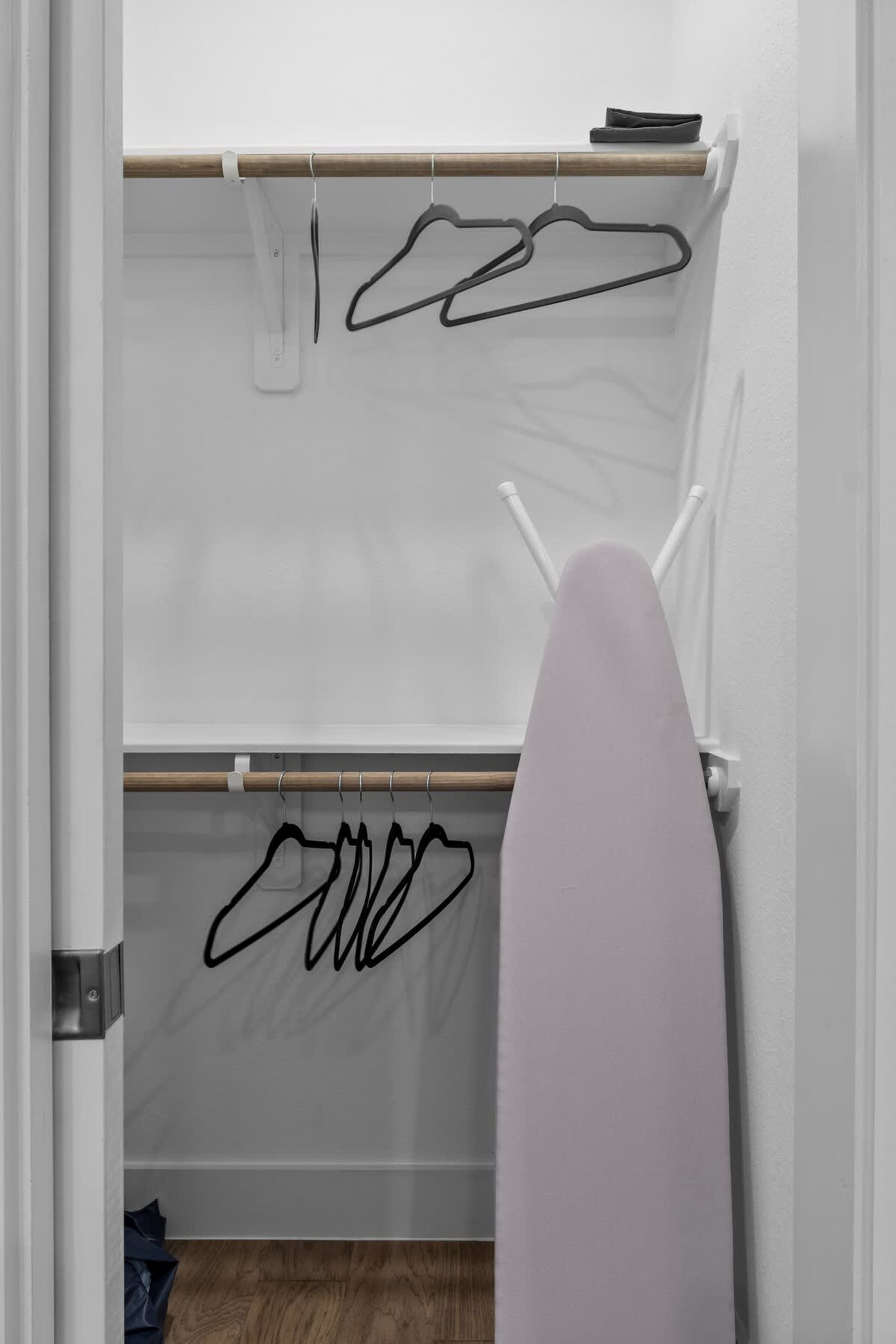 A closet with hanging clothes and an ironing board.