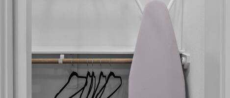 A closet with hanging clothes and an ironing board.