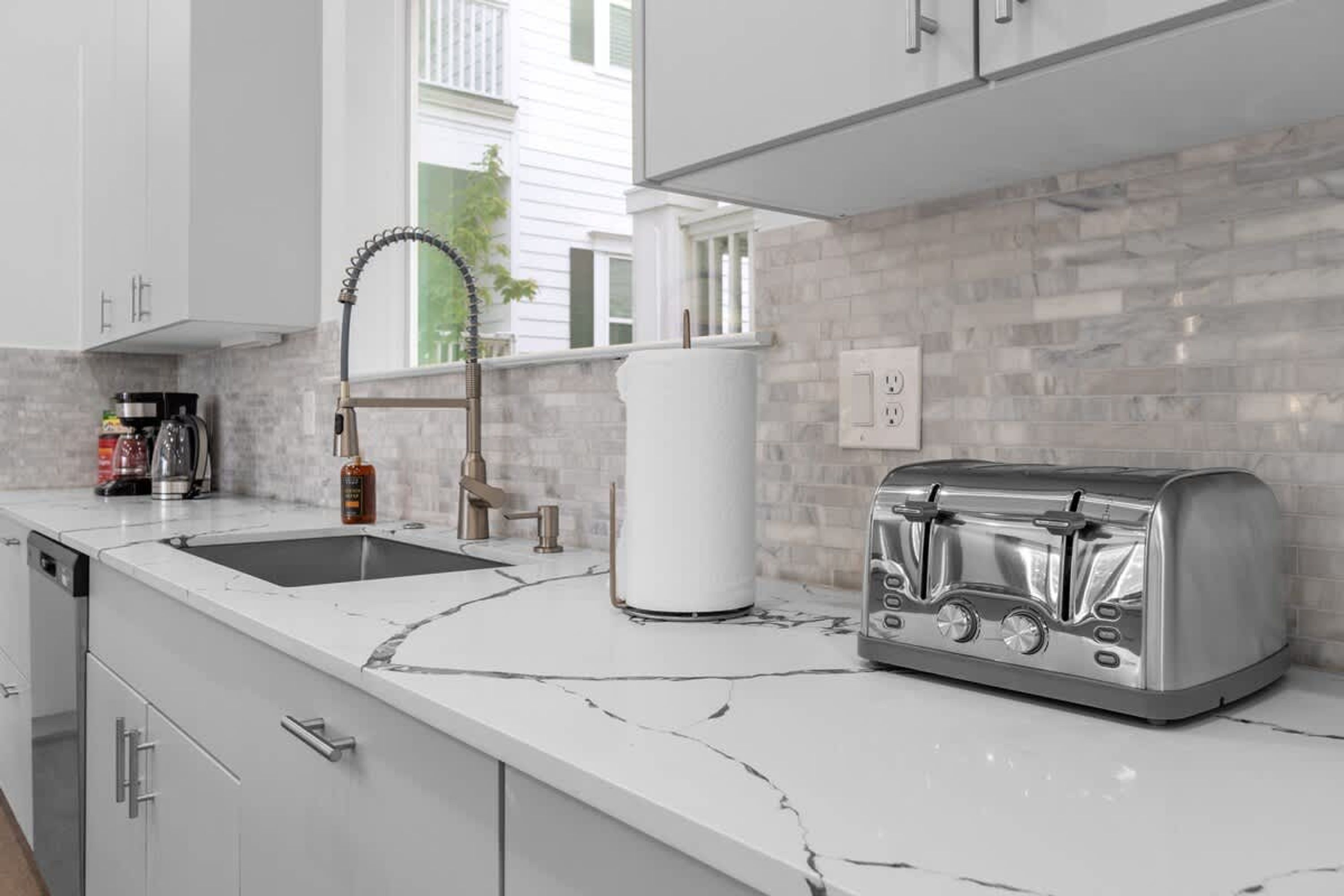 Una cucina moderna con mobili bianchi, un piano di lavoro in marmo, un tostapane integrato e una finestra che si affaccia su una zona residenziale.