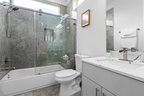 A modern bathroom with a glass-enclosed shower, a white bathtub, a toilet, and a vanity with a mirror. - Downtown Houston 3BR Bachelorette Escape (Houston)
