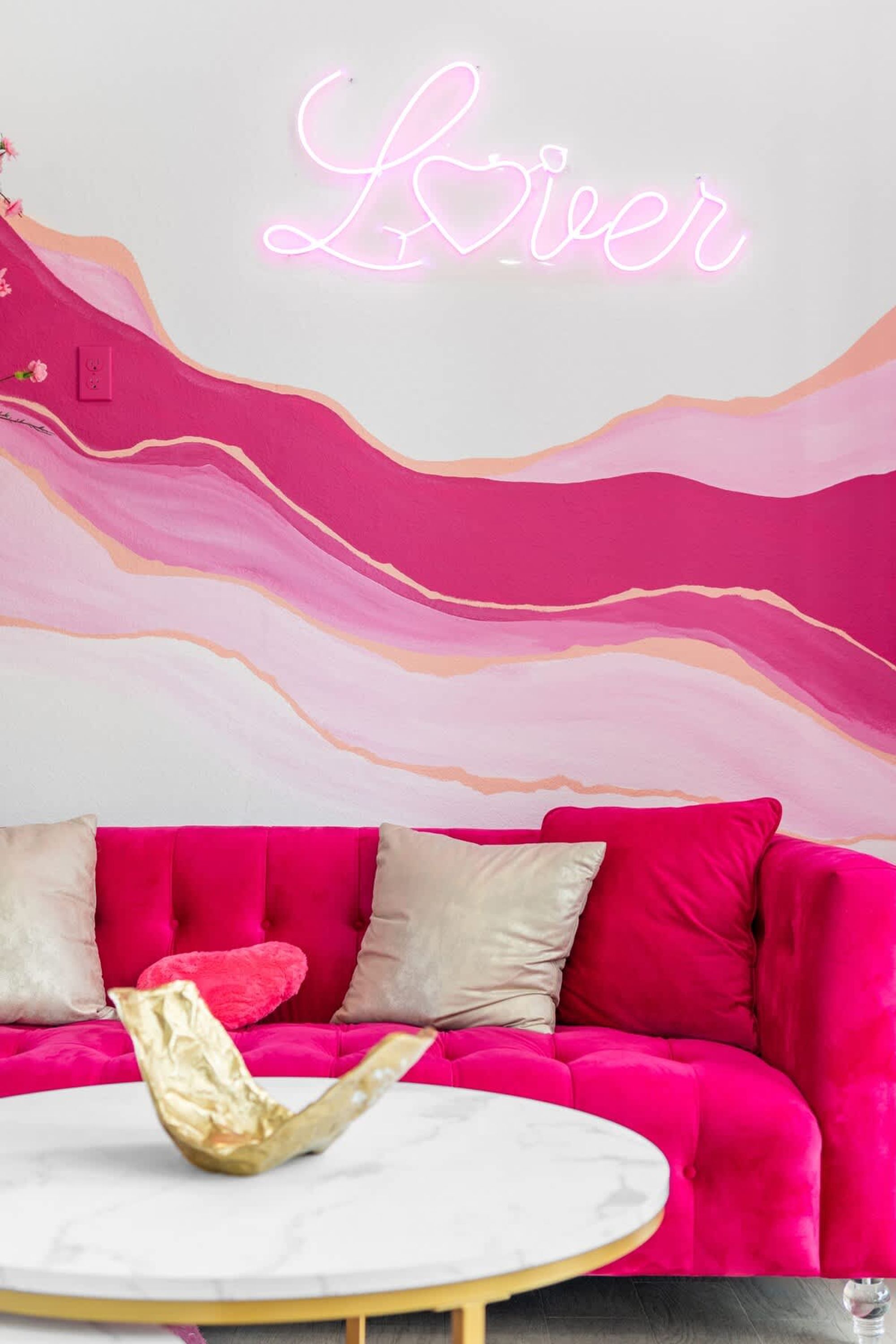 A vibrant room with a pink sofa, a neon sign reading "River," and a marble table.
