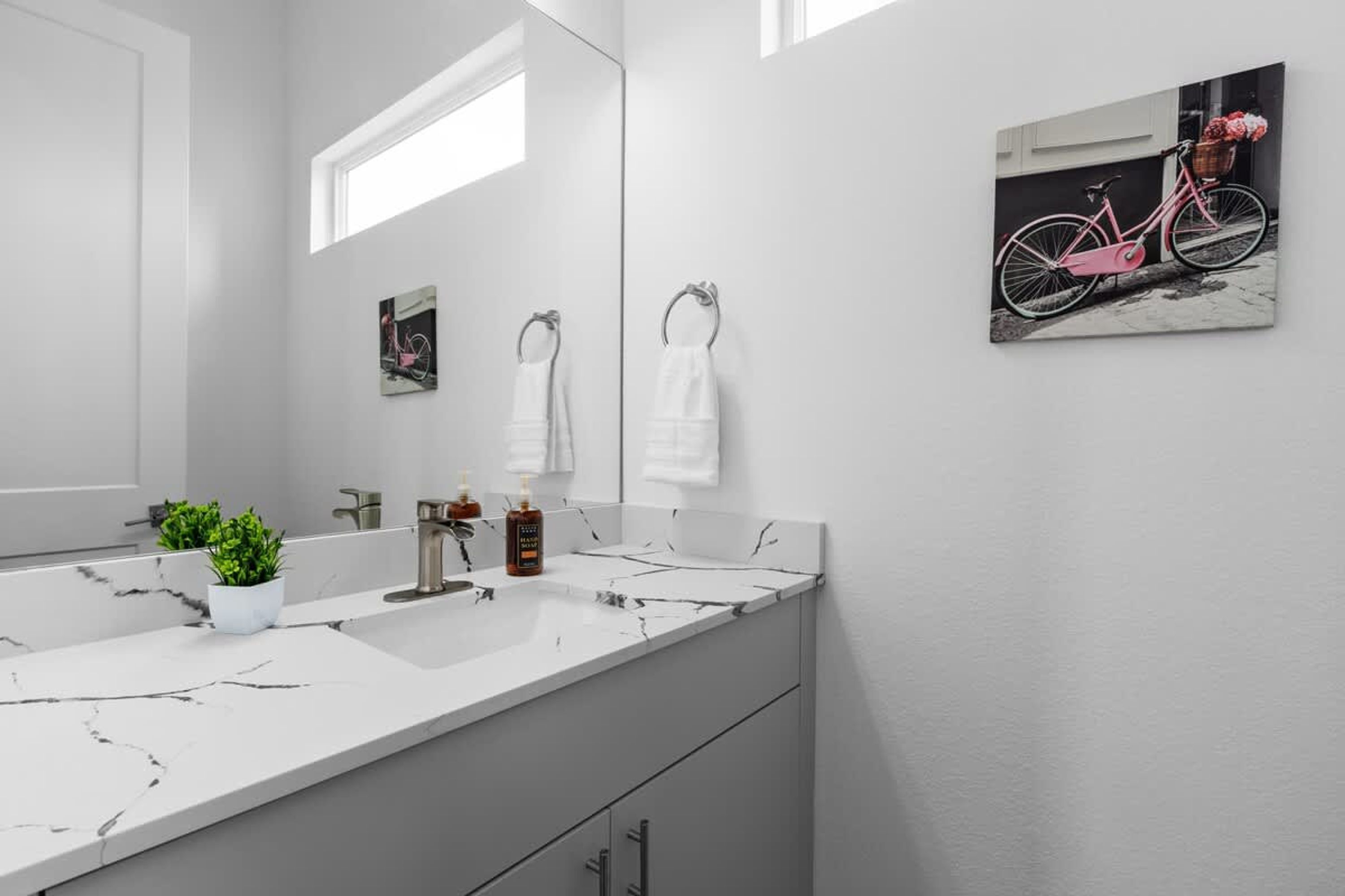 Un baño moderno con un lavamanos de mármol blanco, una planta en maceta y una obra de arte con temática de bicicleta en la pared.