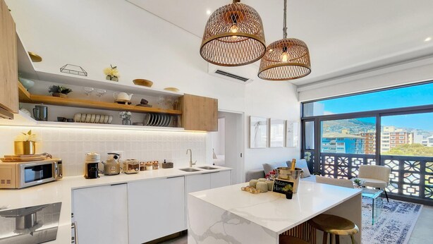 Una cocina moderna con armarios blancos, una isla de mármol e iluminación colgante.