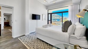 Una habitación de hotel moderna con una cama grande, un televisor, un balcón con vistas a la ciudad y una alfombra estampada.