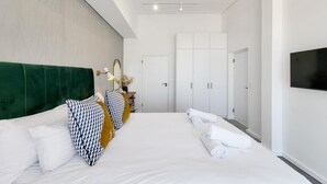 Habitación de hotel moderna con una cama grande, cabecera verde, armario y televisor de pantalla plana.