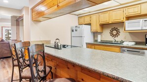 Una cocina con armarios de madera, encimera de granito, refrigerador, microondas y hervidor.