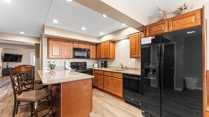 A modern kitchen with wooden cabinets, a black refrigerator, a microwave, and a granite countertop.