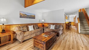 A spacious living room with a wooden ceiling, a large sofa set, a coffee table, and a staircase leading to another level.