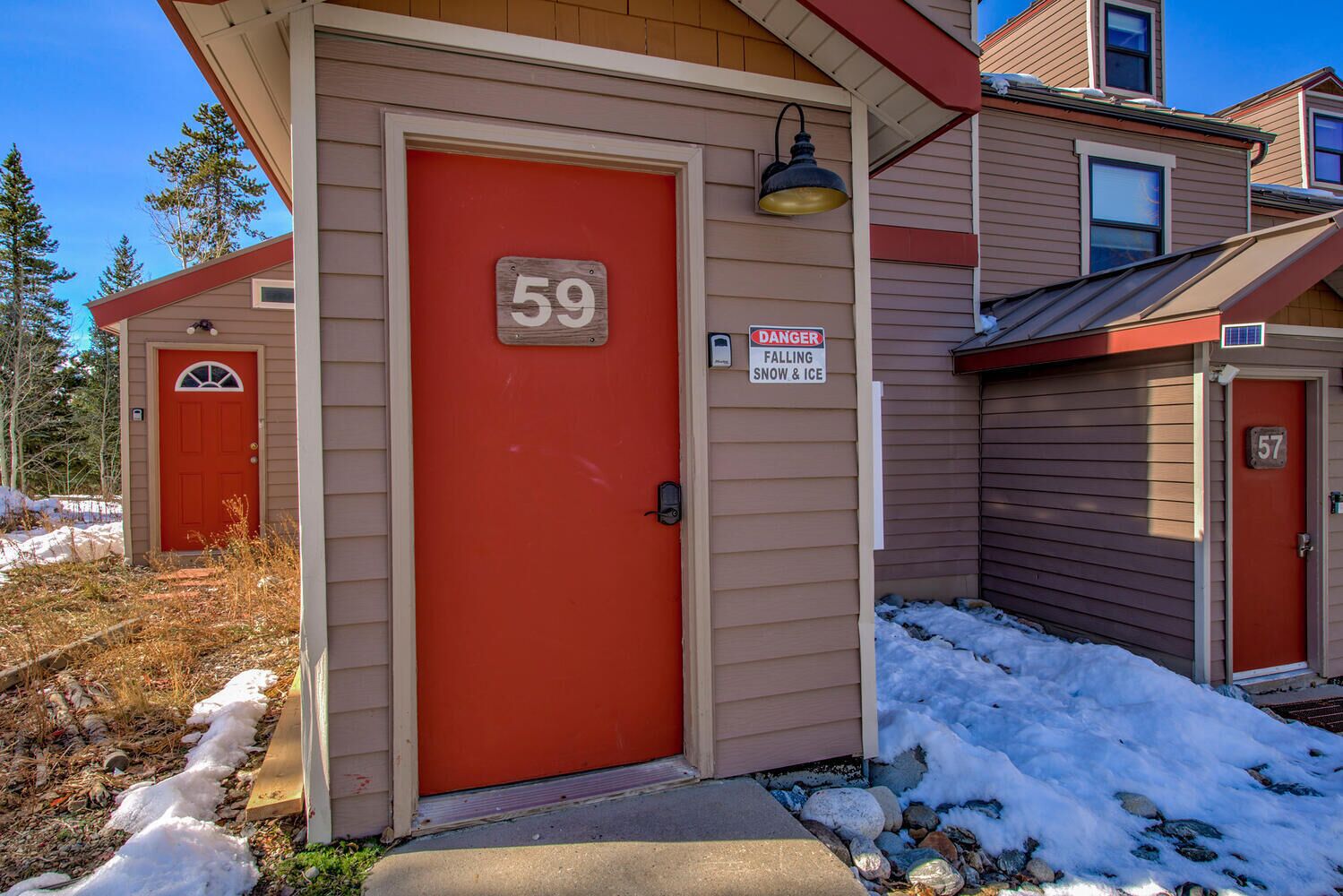 A building with a red door marked with the number 59, a 'DANGER FALLING SNOW & ICE' sign, and a neighboring building with the number 57.