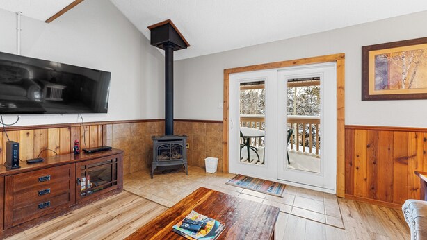 A cozy living room with a wooden cabinet, a TV mounted on the wall, a fireplace, and a sliding glass door leading to a balcony.