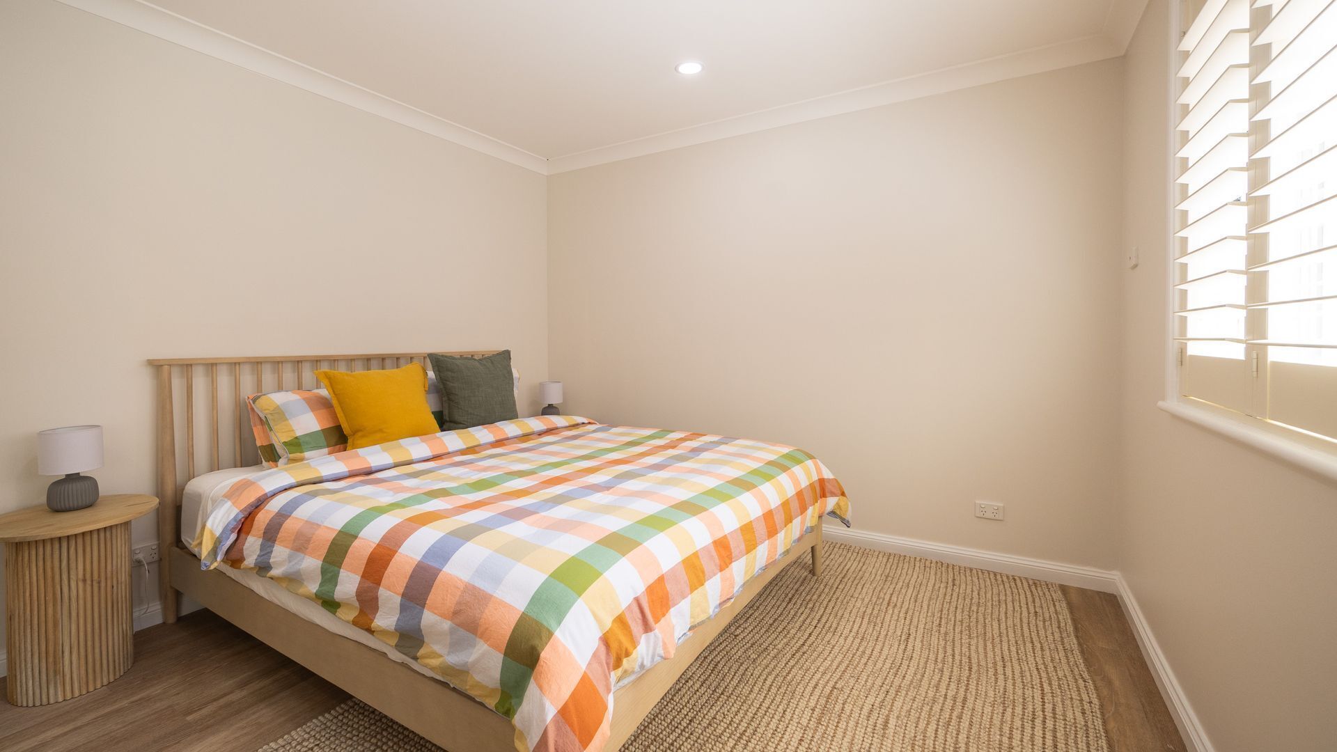 A bedroom with a bed, a nightstand, a lamp, and a window with blinds.